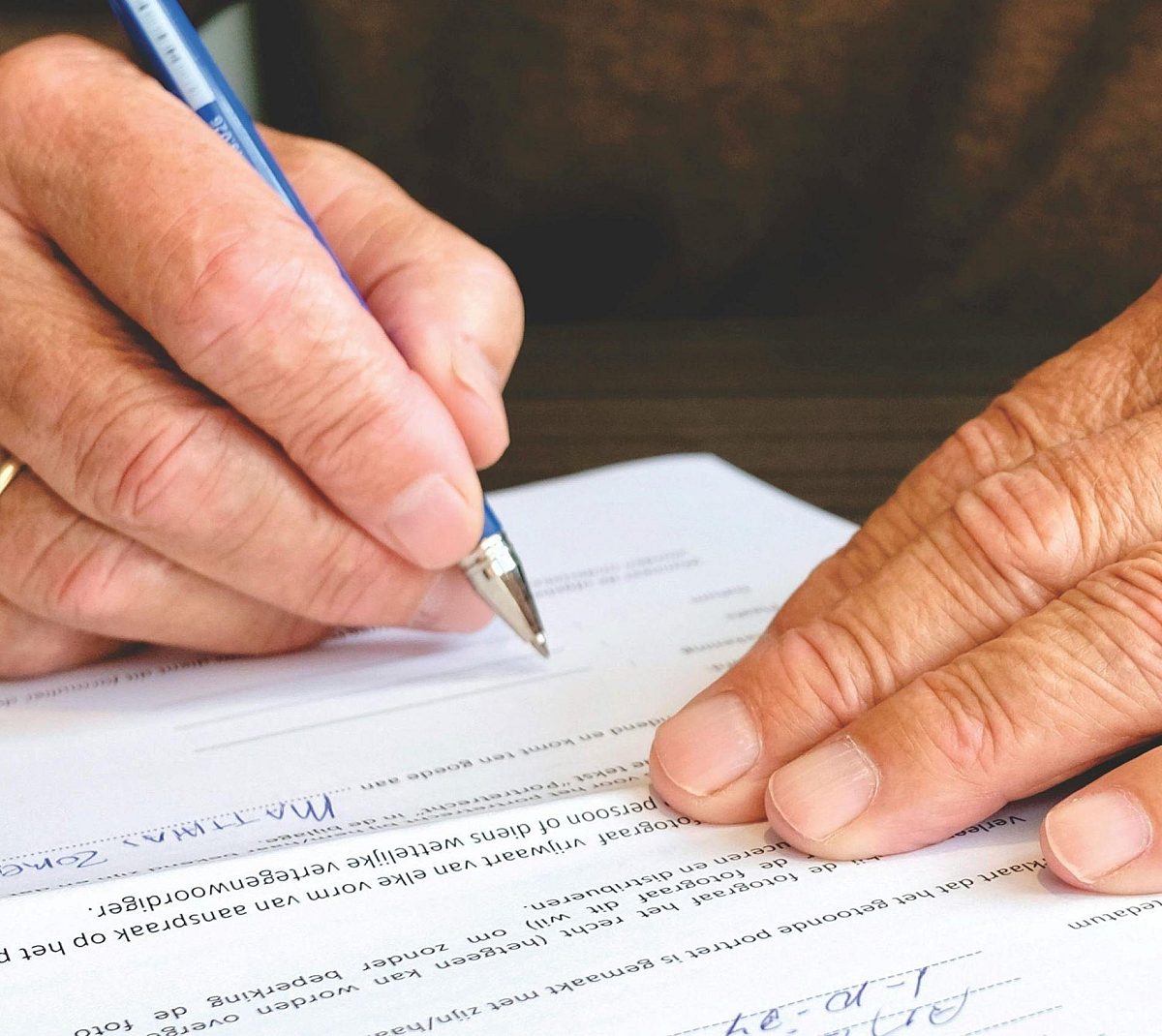 A close up of an older man's hands signing a document.