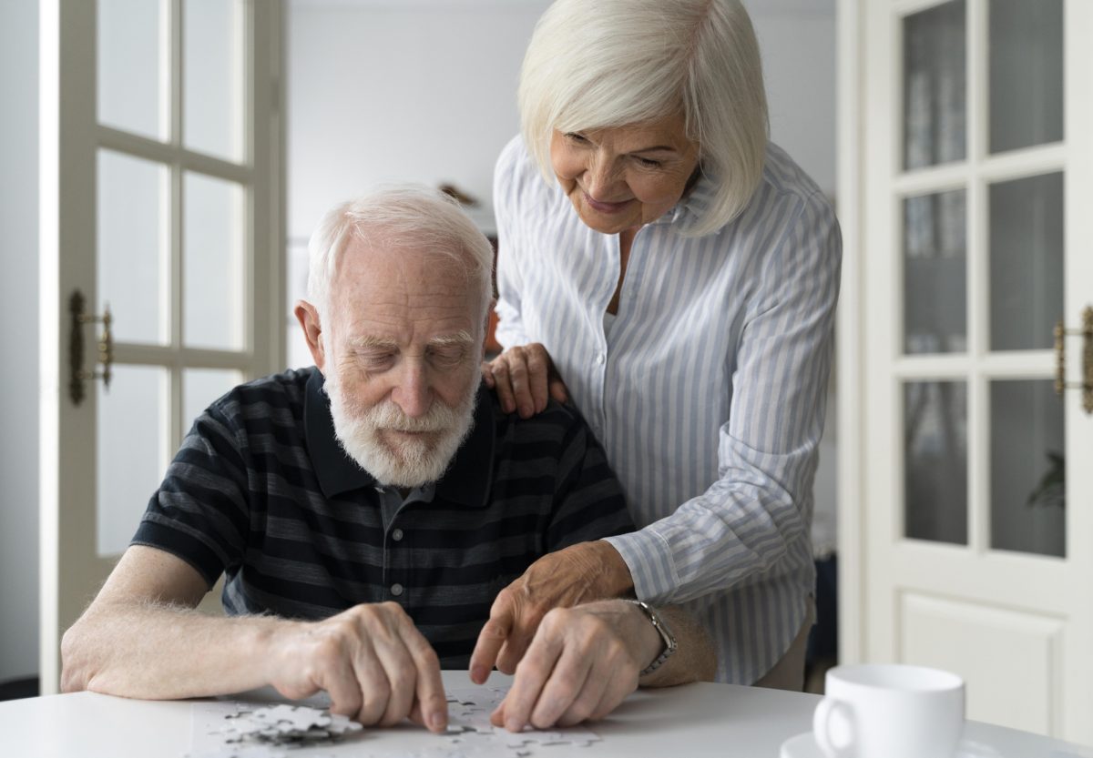 older man with white beard and hair and older woman with white hair working on a puzzle