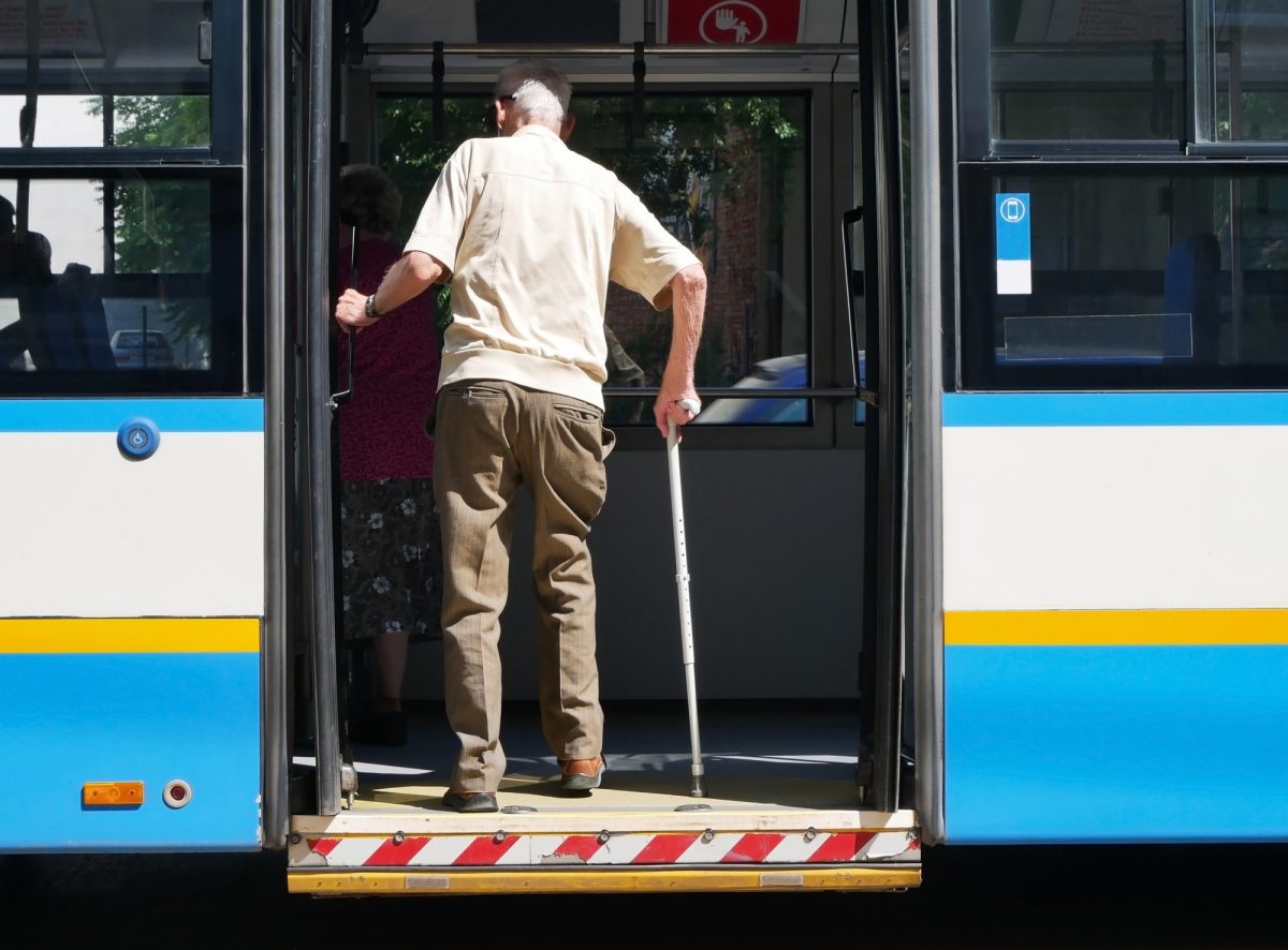 Back of elderly man with walking cane boarding train in khaki pants