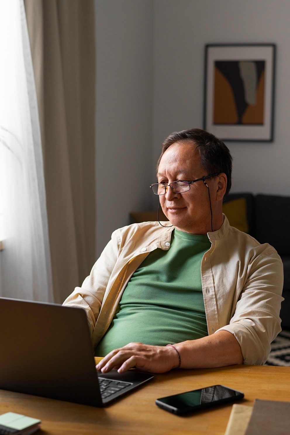 An older man of non-white ethnicity sits at a desk and types on a laptop computer